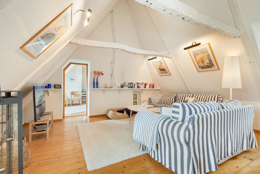 Wohnzimmer mit Dachschräge, gestreiften Sofas, Teppich, TV, Bildern und Bücherregal.