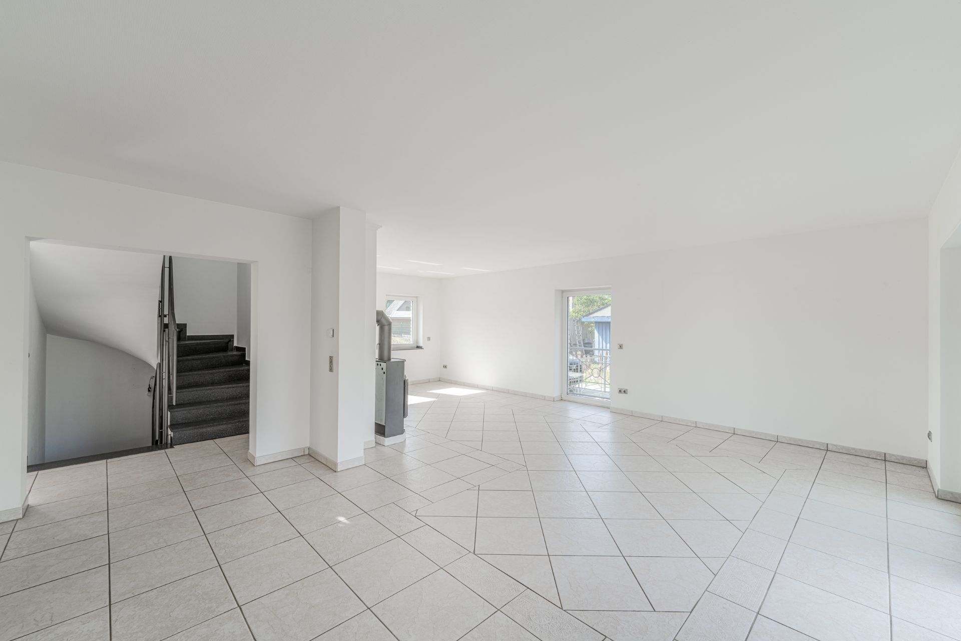 Heller, leerer Raum mit Fliesenboden, Treppe und Zugang zur Terrasse.