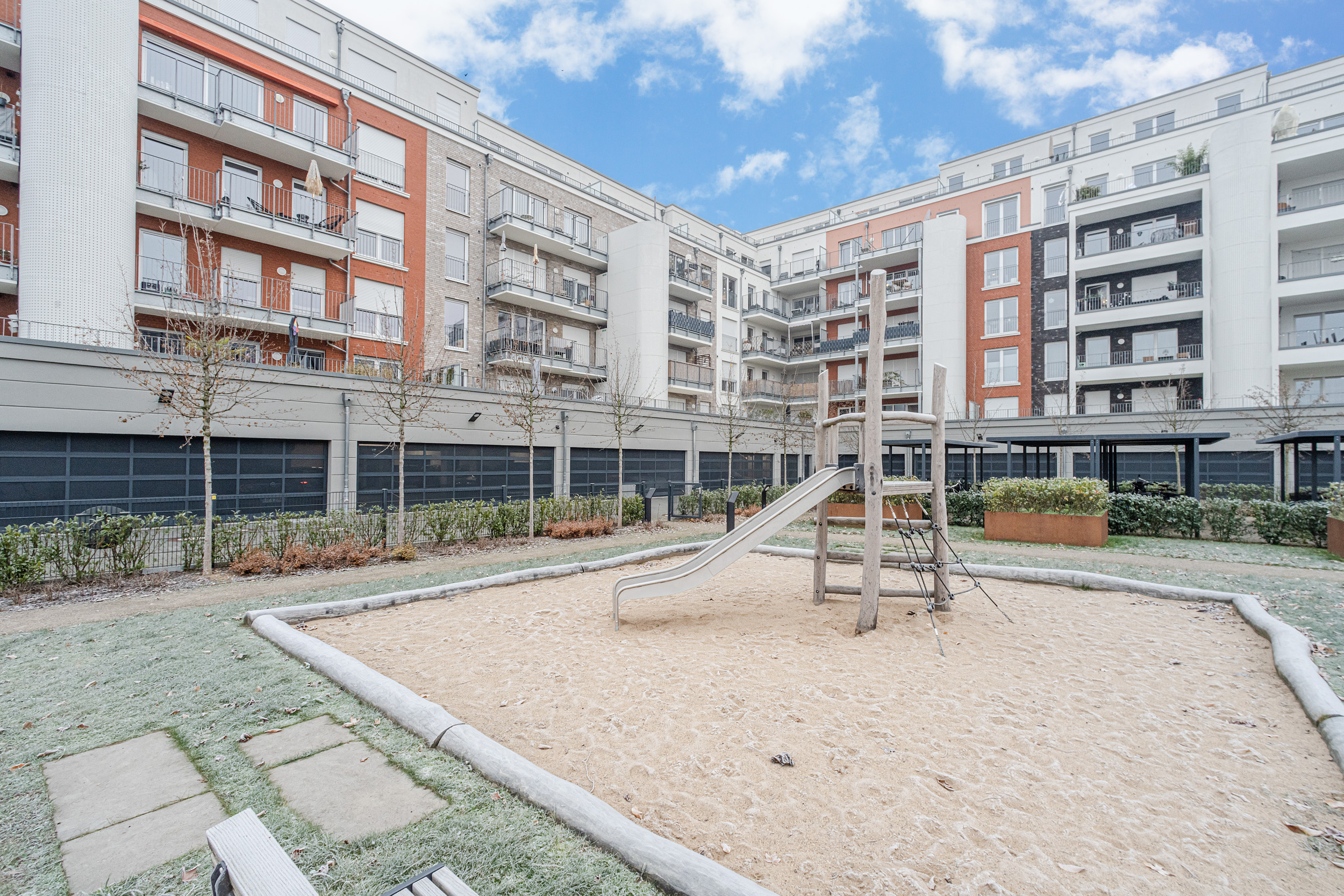Kinderspielplatz mit Rutsche und Sandfläche in einem Innenhof mit Mehrfamilienhäusern.