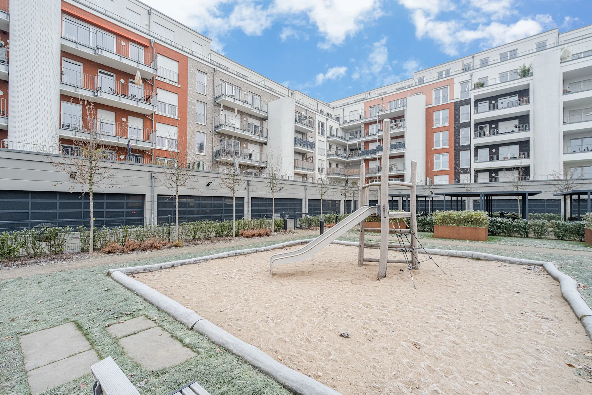 Kinderspielplatz mit Rutsche und Sandfläche in einem Innenhof mit Mehrfamilienhäusern.