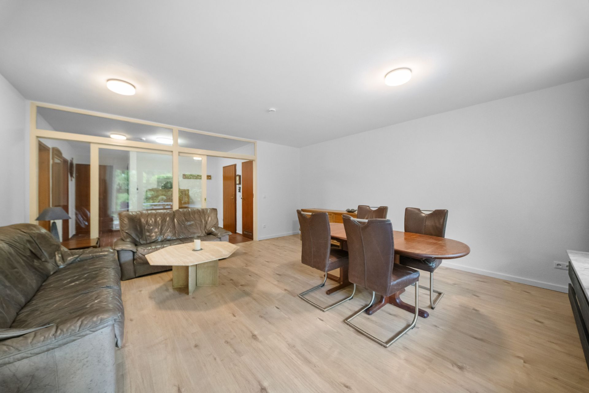 Wohnzimmer mit Ledersofas, Holztisch und Essbereich mit sechs Stühlen auf hellem Holzboden.