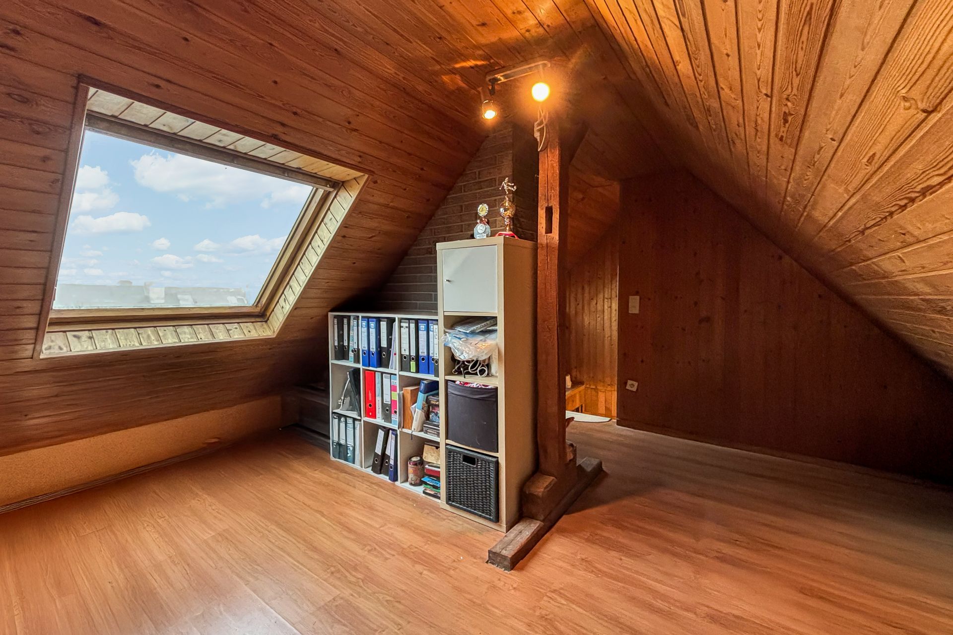 Dachgeschossraum mit Holzverkleidung, großem Dachfenster und Regal mit Ordnern.