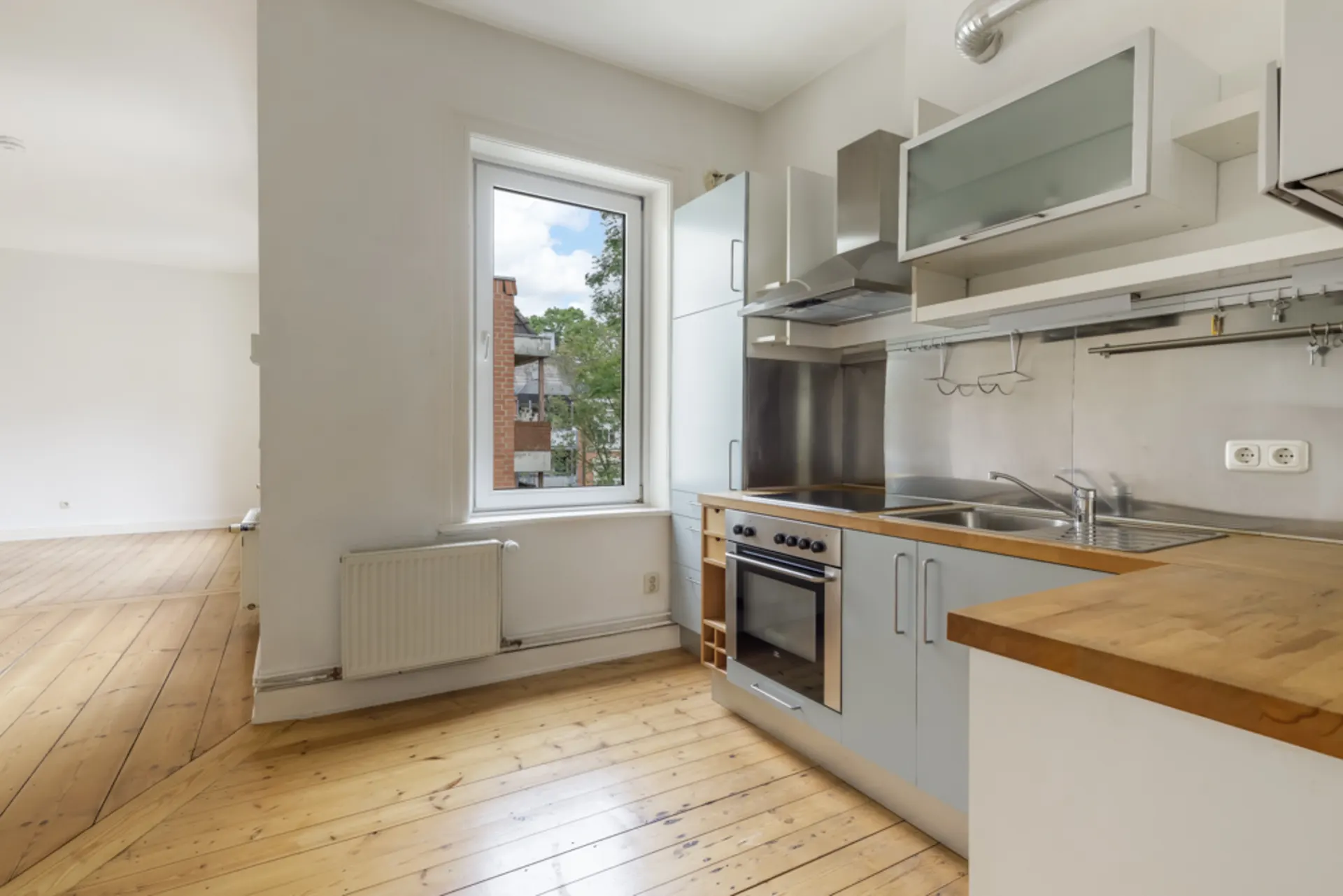 Moderne Einbauküche mit Holzarbeitsplatte und großem Fenster, angrenzend an einen hellen Wohnbereich.