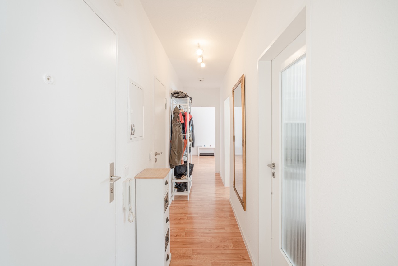 Heller Flur mit Holzboden, großem Spiegel, Garderobe und weißen Türen.