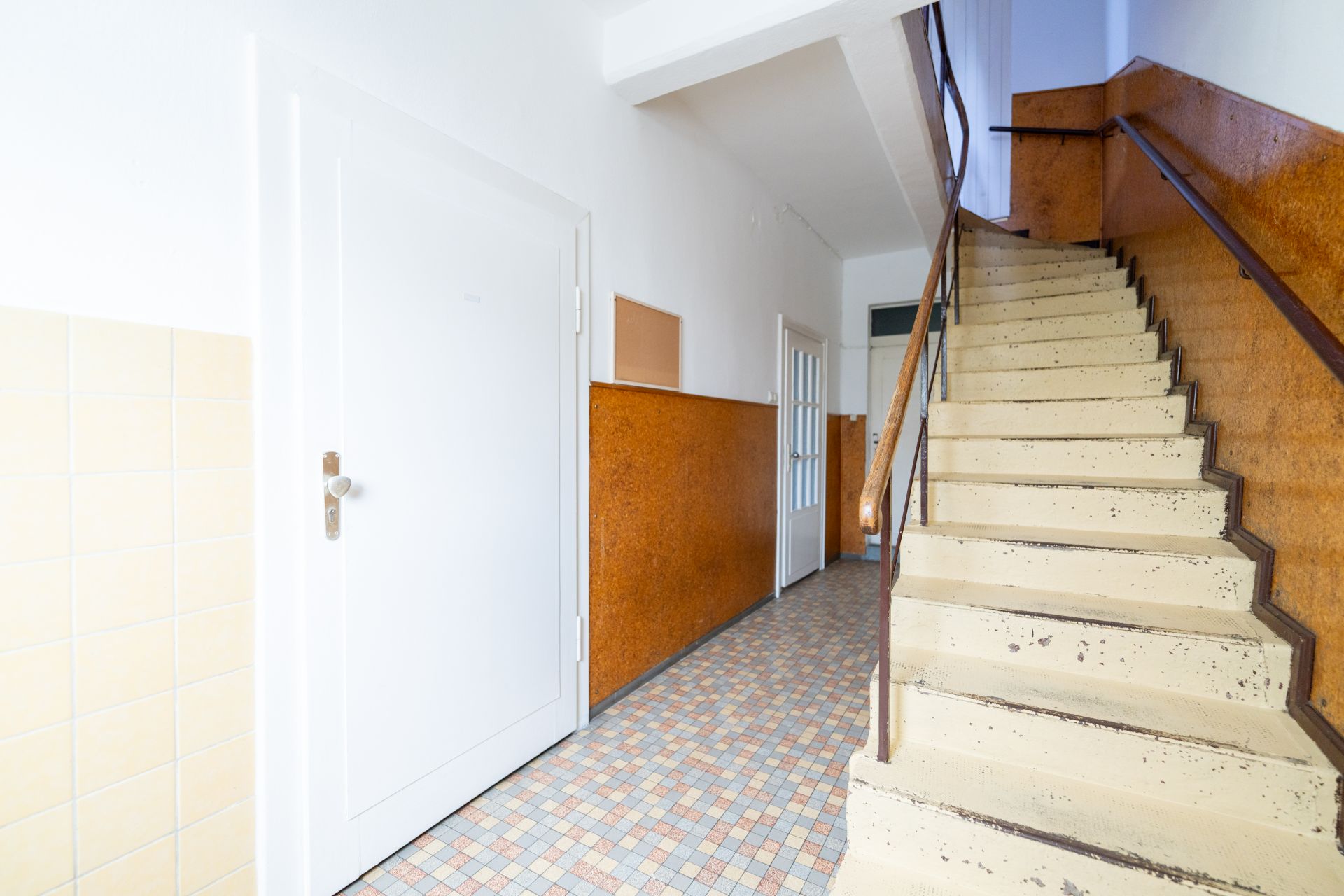 Treppenhaus mit beigem Fliesenboden, brauner Wandverkleidung und weißen Türen.
