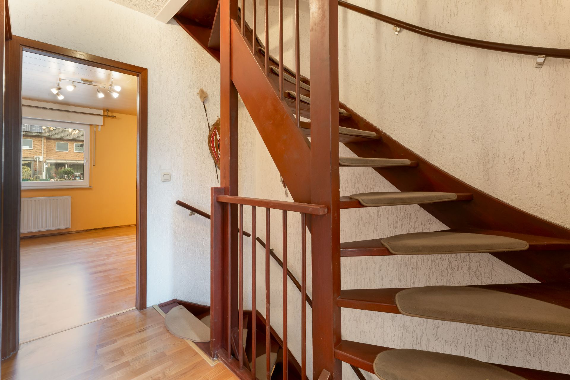 Holztreppe im Flur, daneben Eingang zu einem Raum mit Holzfußboden und Fenster.