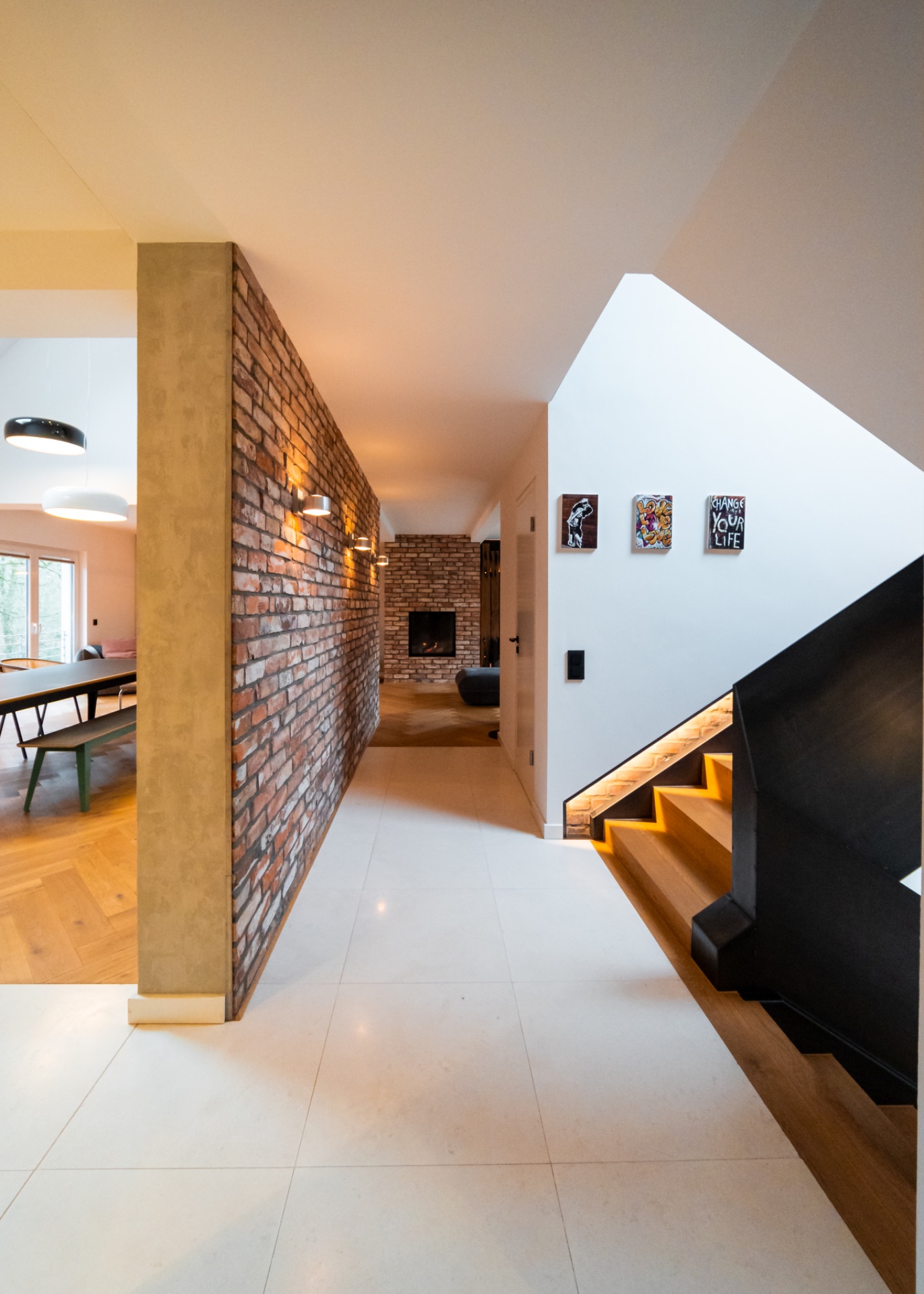 Moderner Flur mit Ziegelwand, Holztreppe und Kamin im Hintergrund.