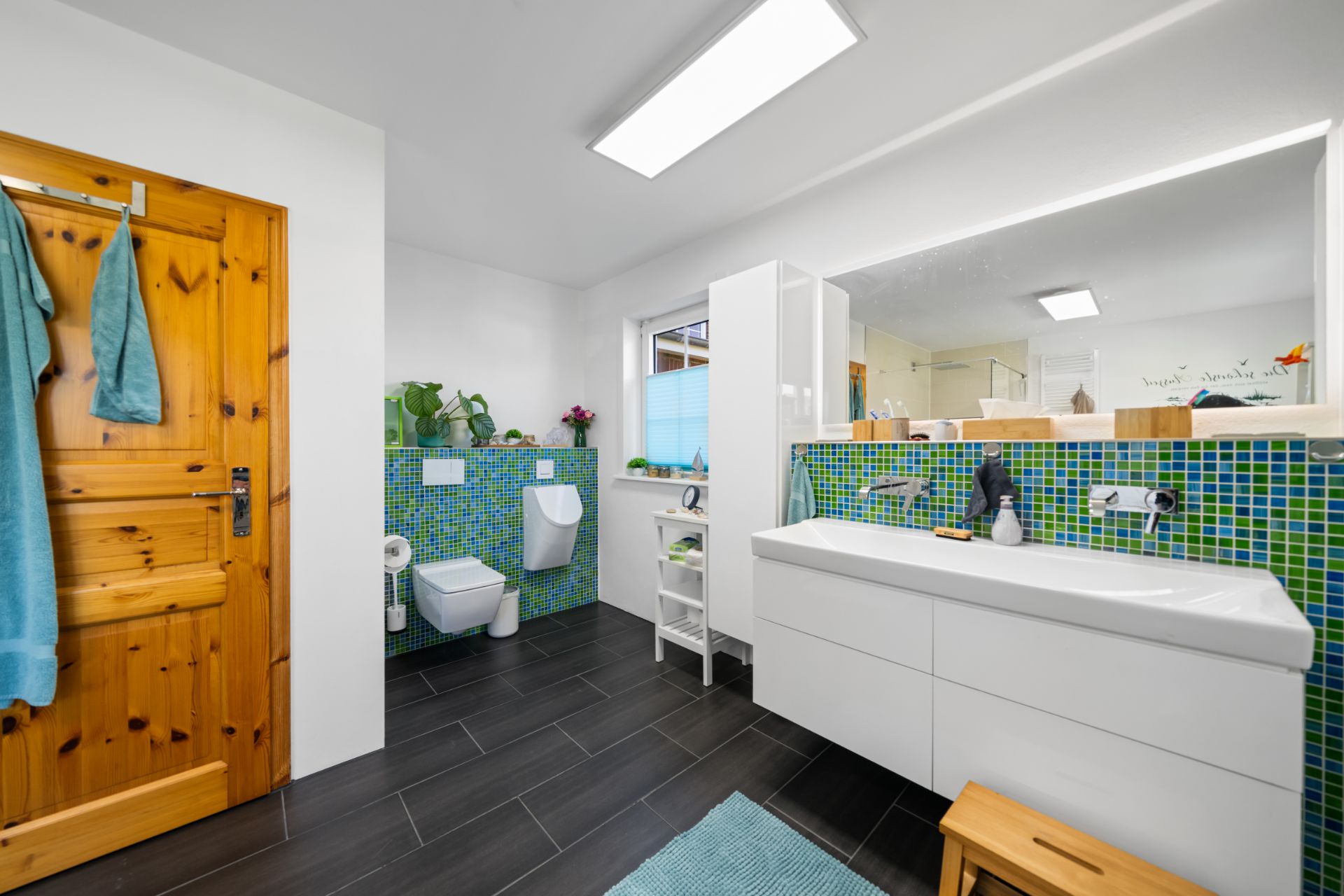 Modernes Badezimmer mit Holz­tür, Doppelwaschtisch, grün-blauen Fliesen und dunklem Fliesenboden.