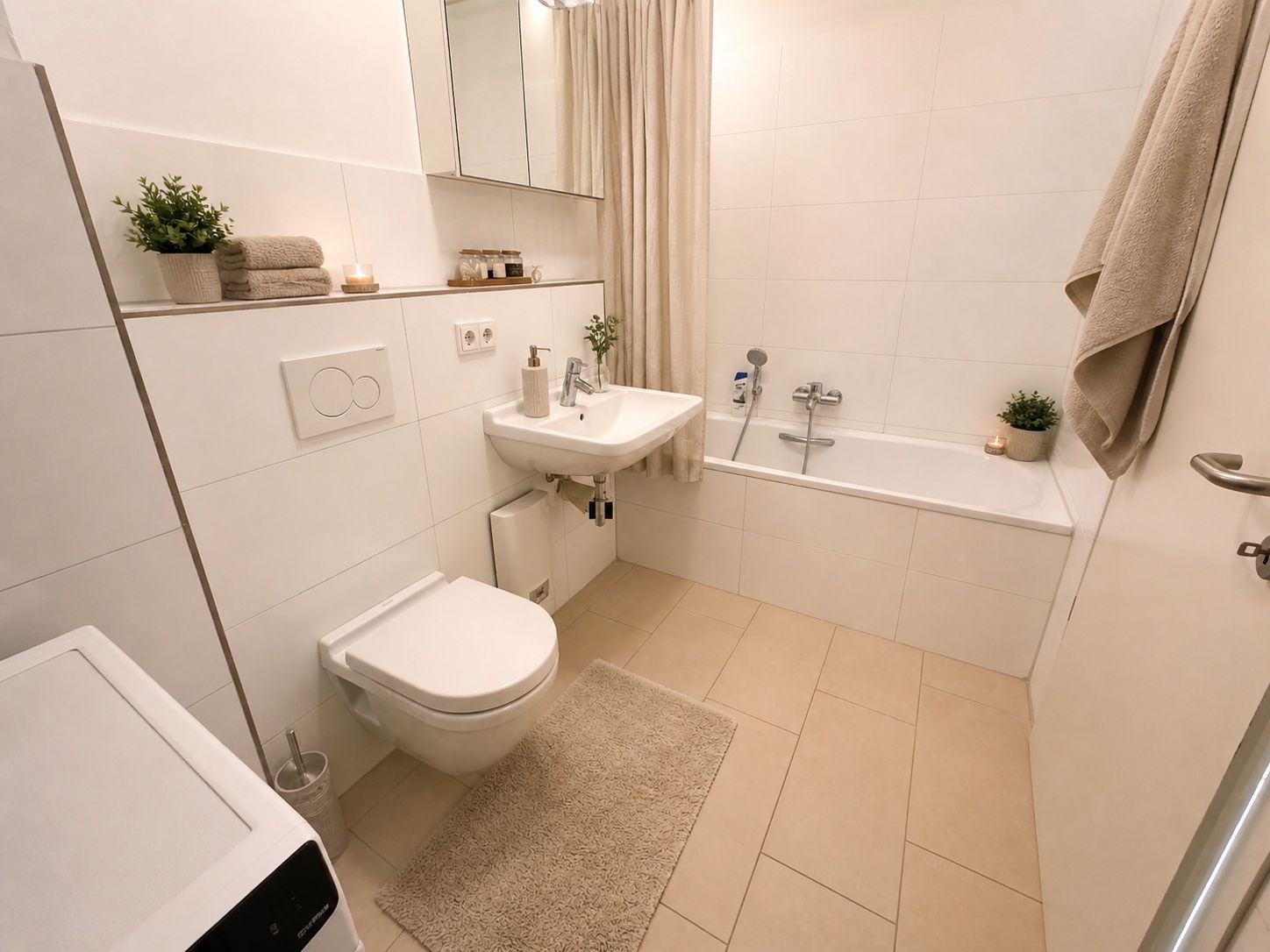Modernes Badezimmer mit Badewanne, WC, Waschbecken, Waschmaschine und beigen Fliesen.