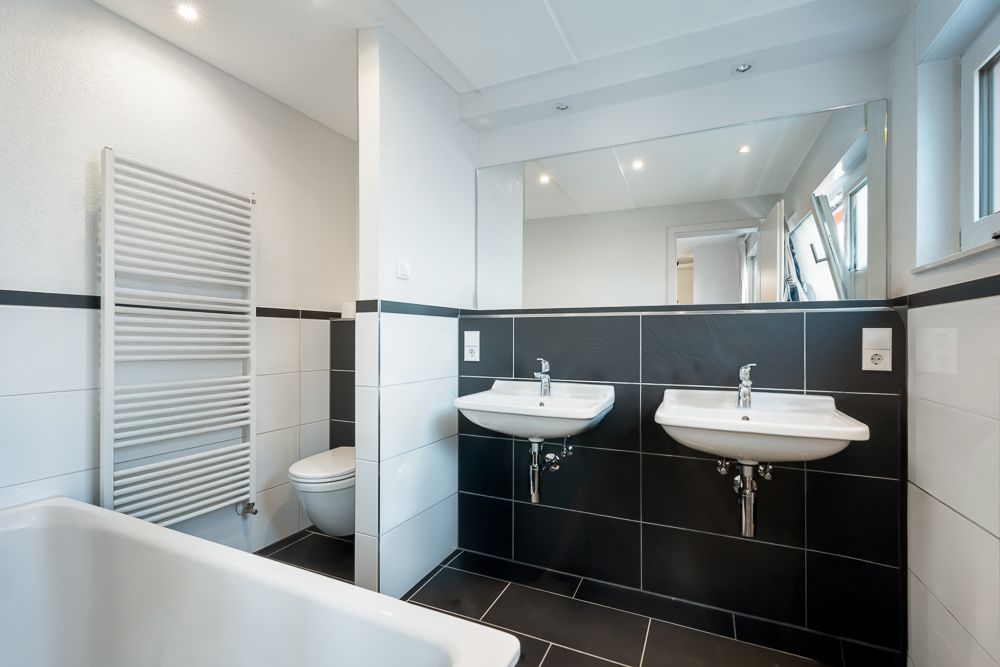 Modernes Badezimmer mit zwei Waschbecken, Badewanne, WC und großem Spiegel.