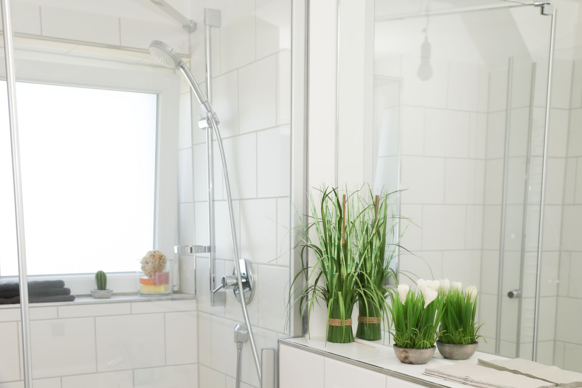 Modernes Badezimmer mit Dusche, weißen Fliesen und Pflanzen auf dem Waschbeckenrand.