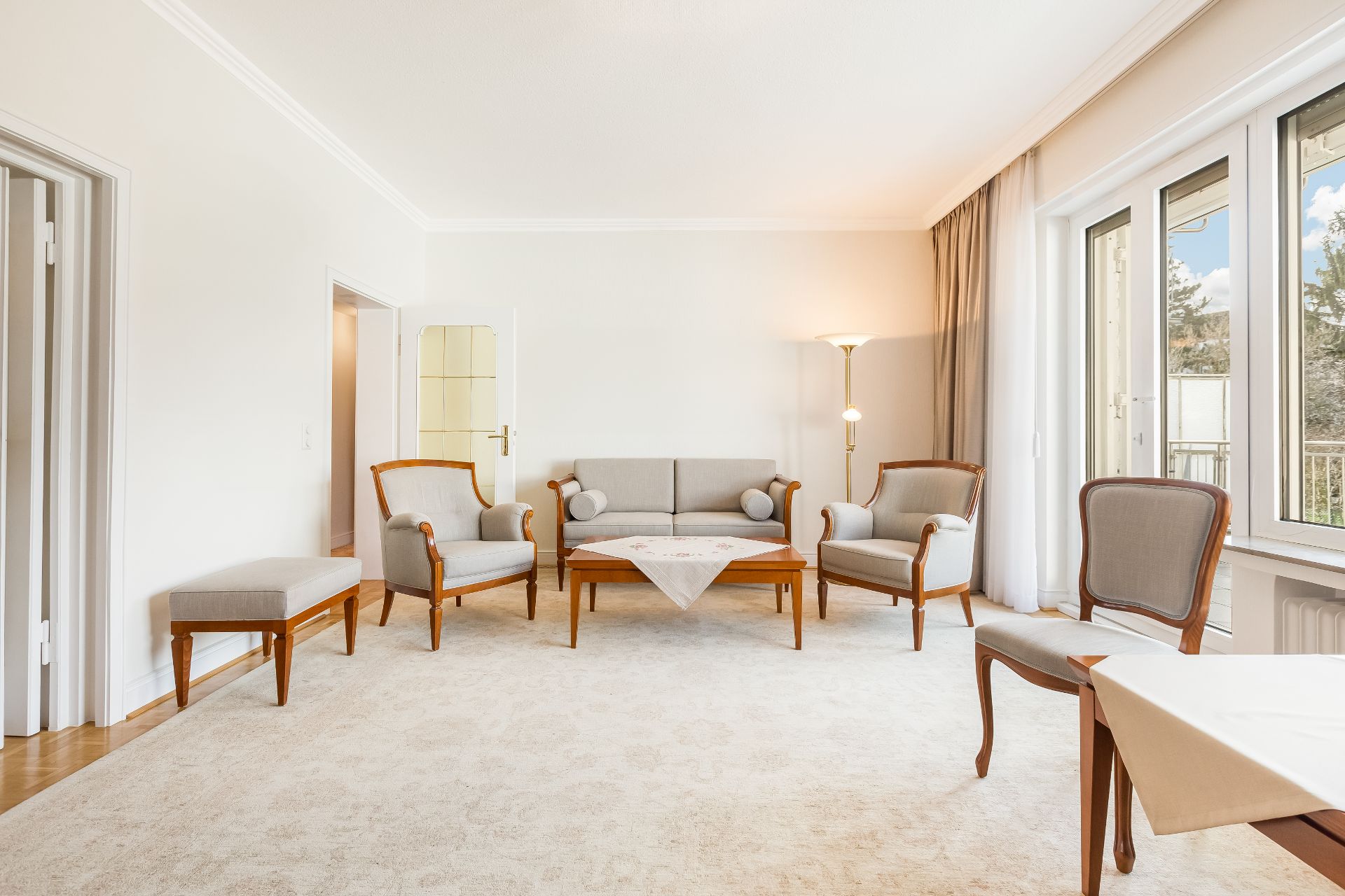 Helles Wohnzimmer mit Sitzgruppe, Teppich, Stehlampe und großen Fenstern.