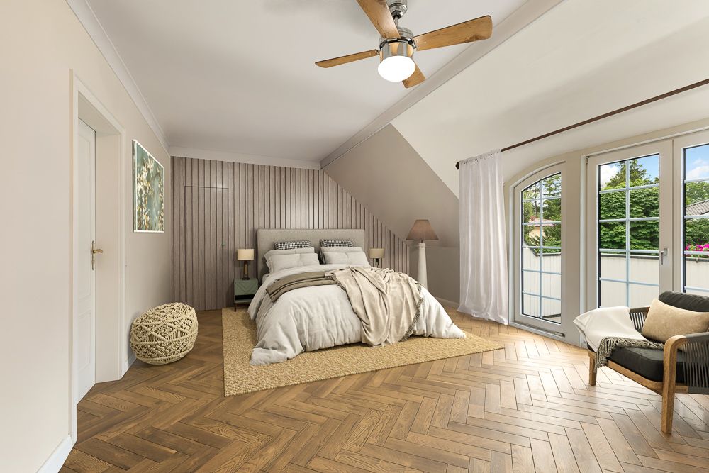 Helles Schlafzimmer mit Doppelbett, Deckenventilator, Sessel, Holzfußboden und großen Fenstern mit Blick ins Grüne.