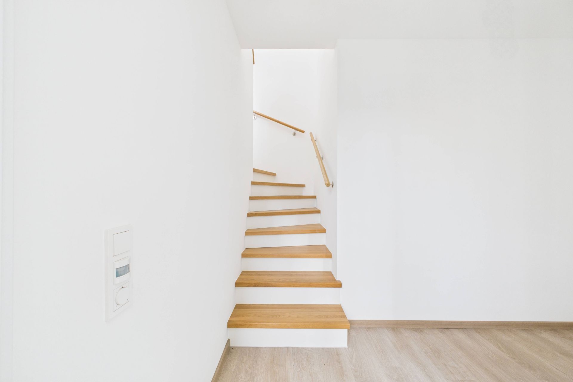 Eine moderne Holztreppe mit weißem Geländer in einem hellen Flur.