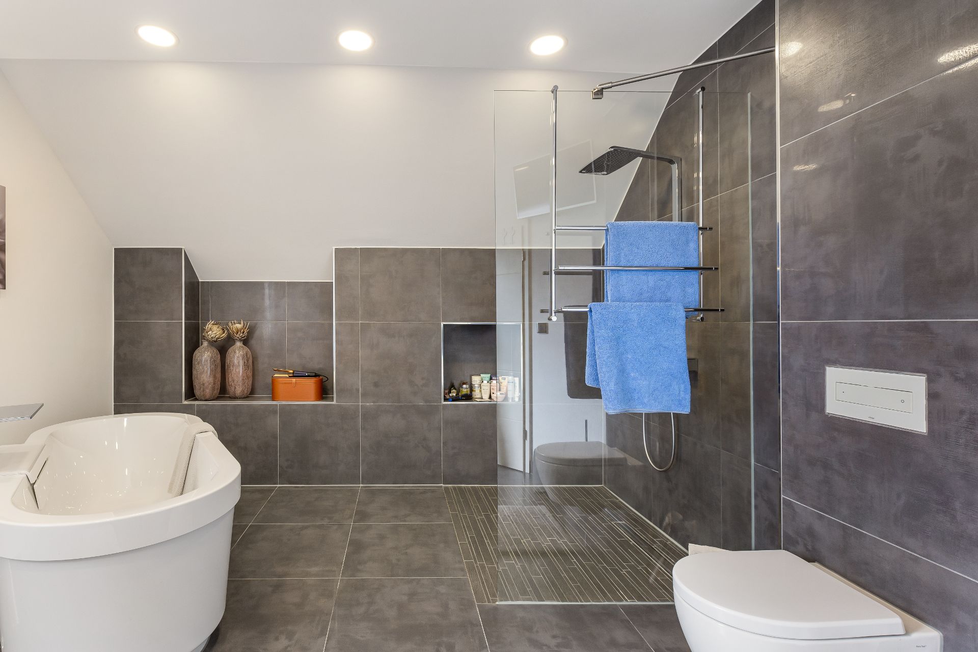 Modernes Badezimmer mit freistehender Badewanne, offener Dusche und grauen Fliesen.