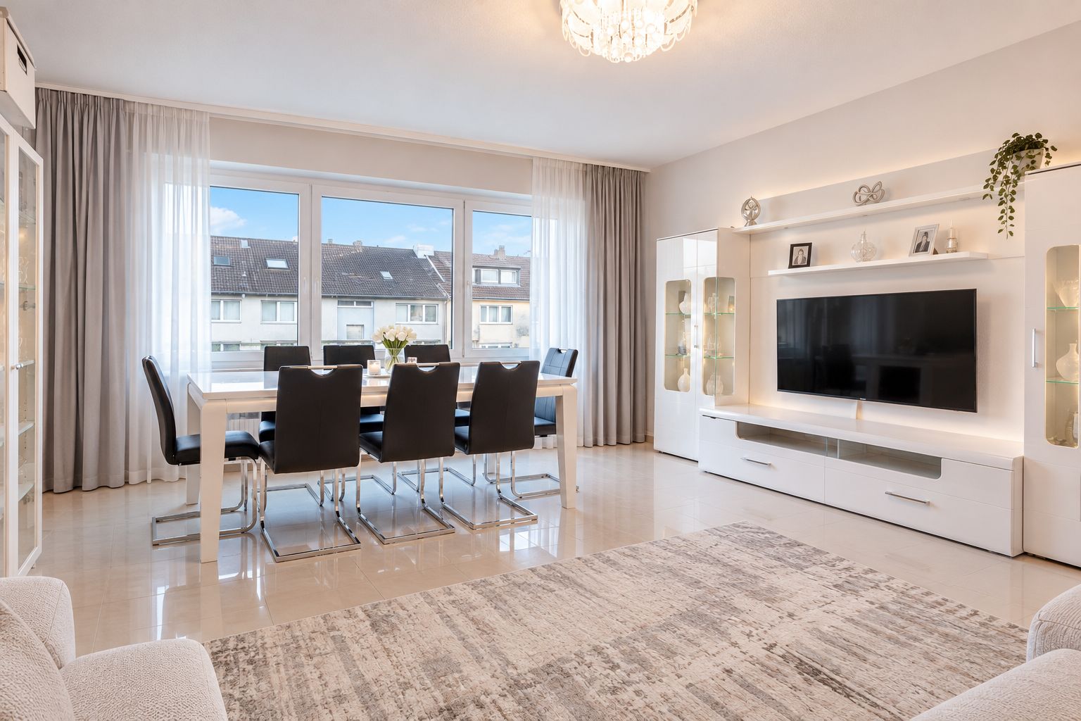 Helles Wohnzimmer mit Esstisch, acht Stühlen, großem Fenster und modernem TV-Möbel.