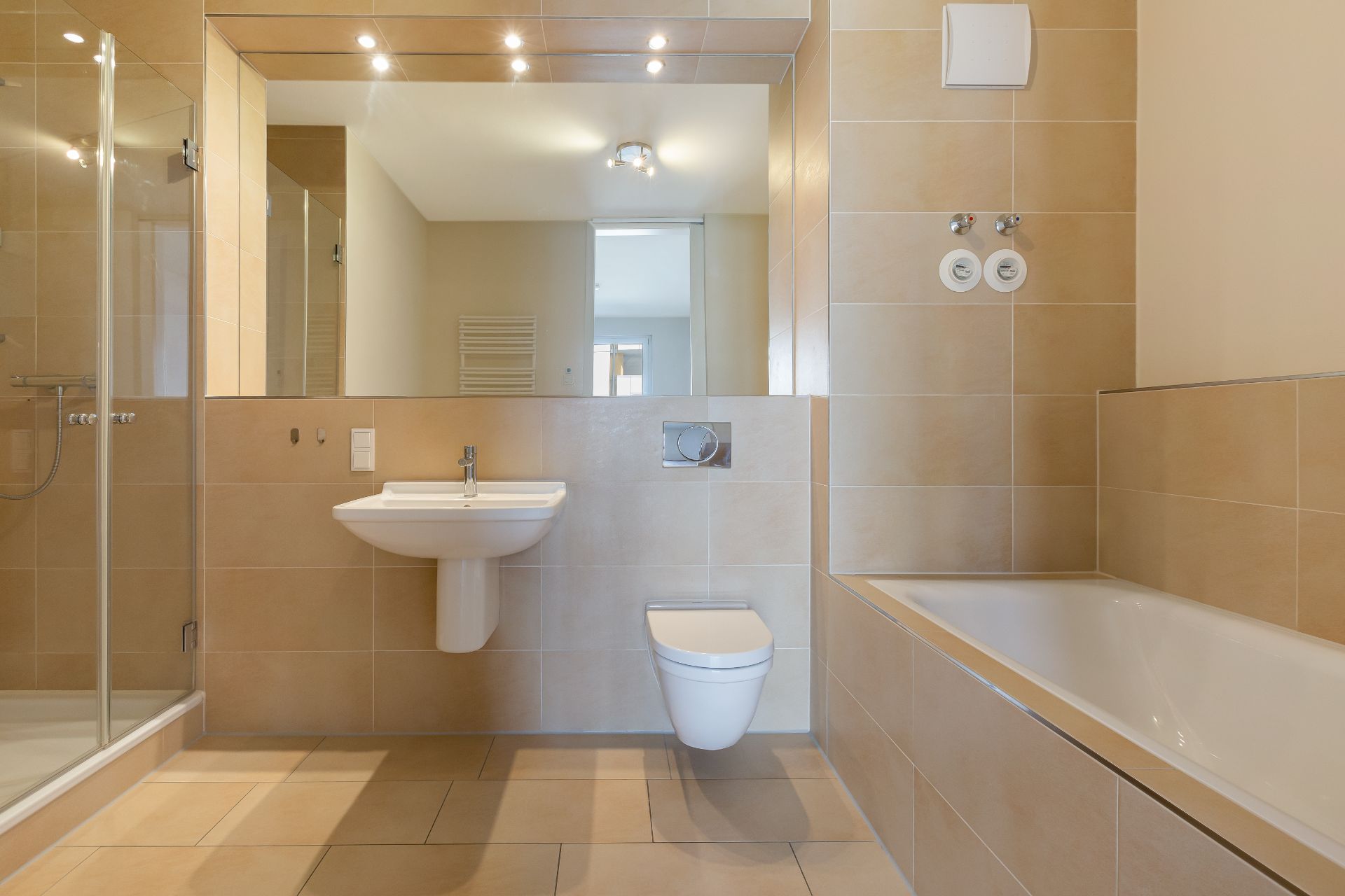 Modernes Badezimmer mit Dusche, Waschbecken, Toilette und Badewanne, große beige Fliesen.