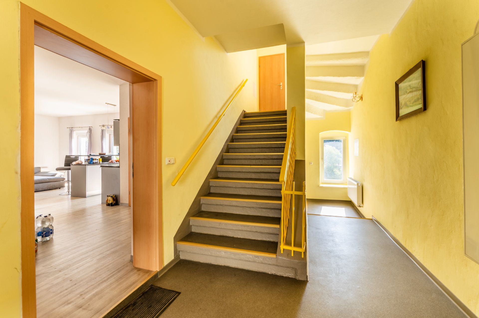 Heller Flur mit gelben Wänden, Treppe und Blick in ein Wohnzimmer mit Holzboden.