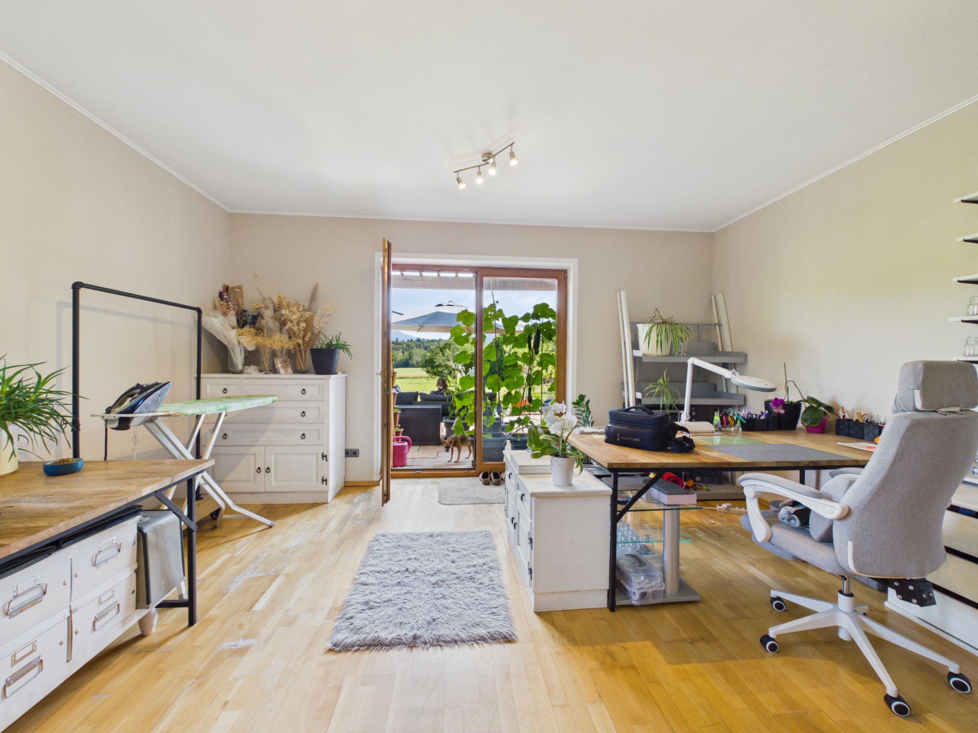 Helles Arbeitszimmer mit Schreibtischen, Stuhl, Pflanzen und Zugang zu einer Terrasse mit Ausblick.