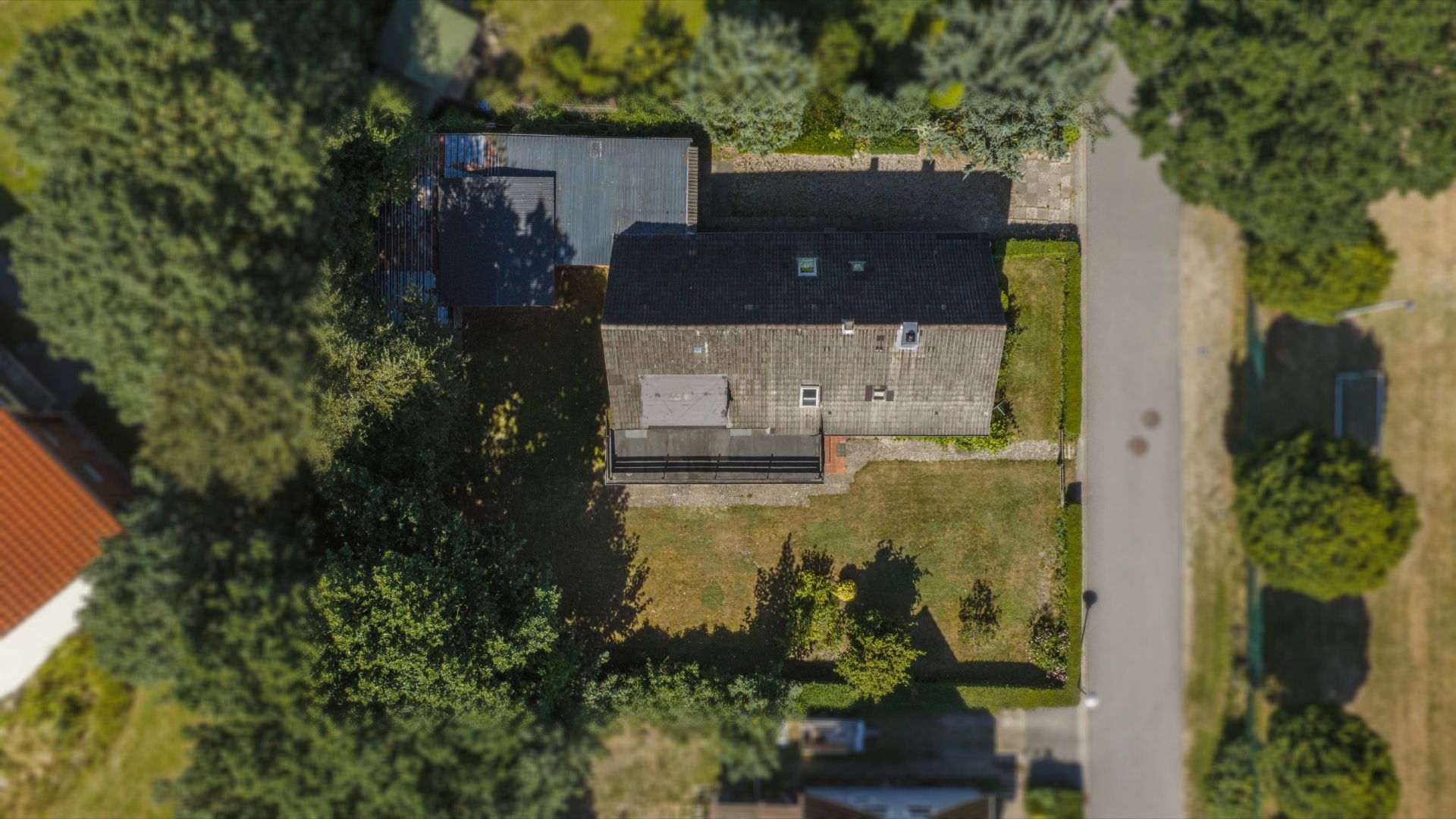 Luftaufnahme eines Hauses mit Garten und angrenzender Straße, umgeben von Bäumen.