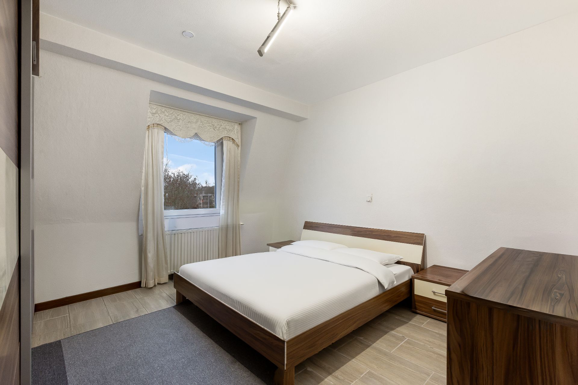 Schlafzimmer mit Doppelbett, Nachttischen und Fenster mit Vorhängen.