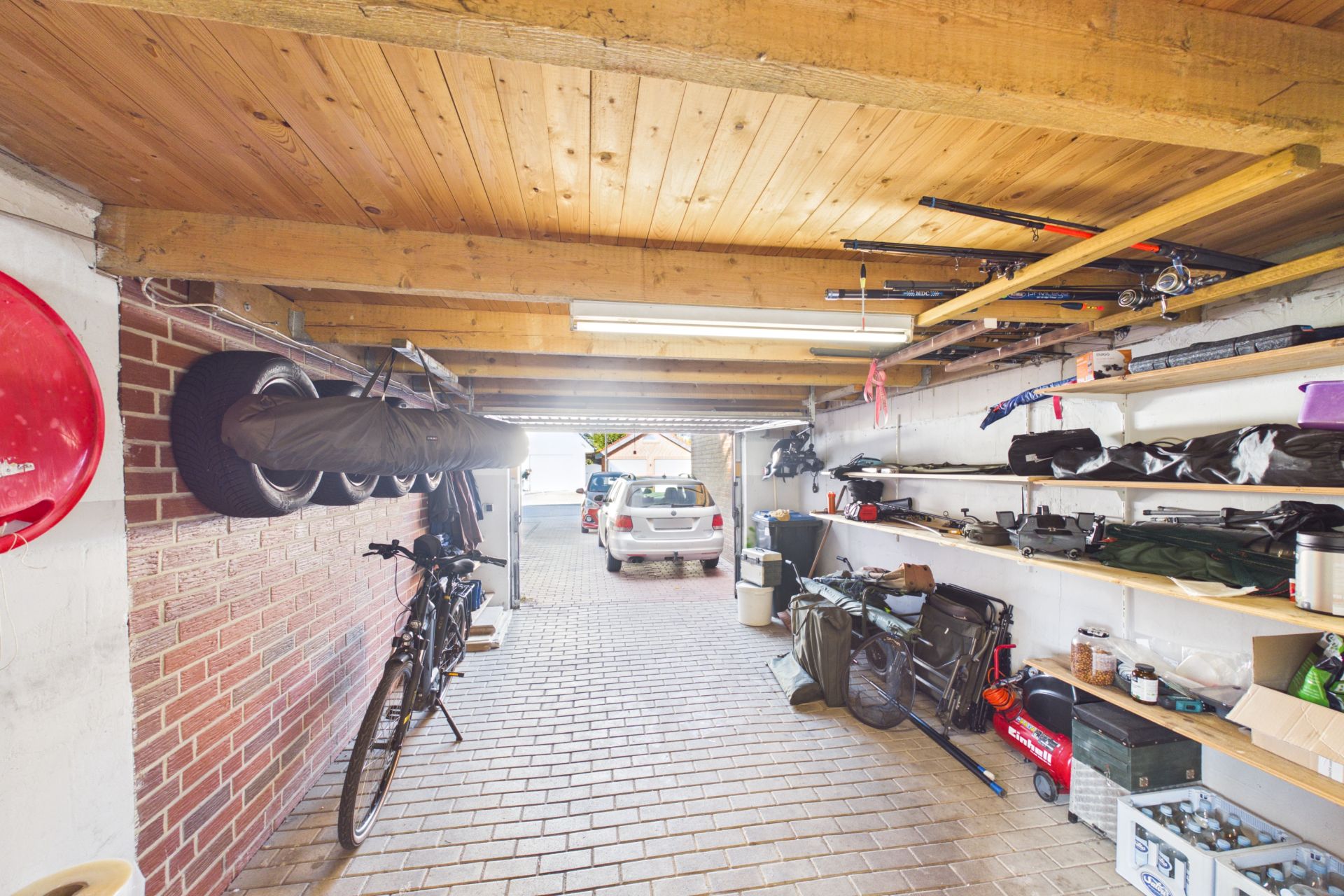 Garage mit Regalen, Werkzeugen, Fahrrad und geparktem Auto im Hintergrund.