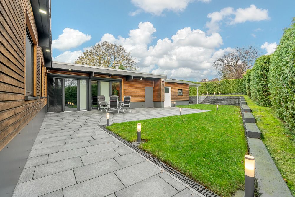 Moderne Terrasse mit Garten, Rasenfläche und Gartenmöbeln, umgeben von Hecken.