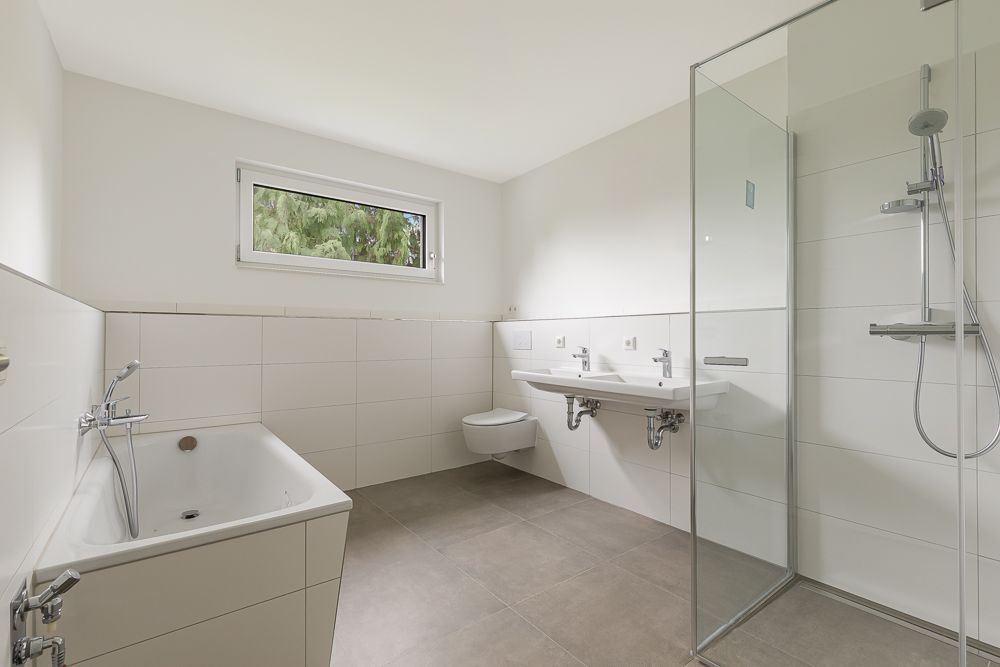 Modernes Badezimmer mit Badewanne, Dusche, zwei Waschbecken, Toilette und Fenster.