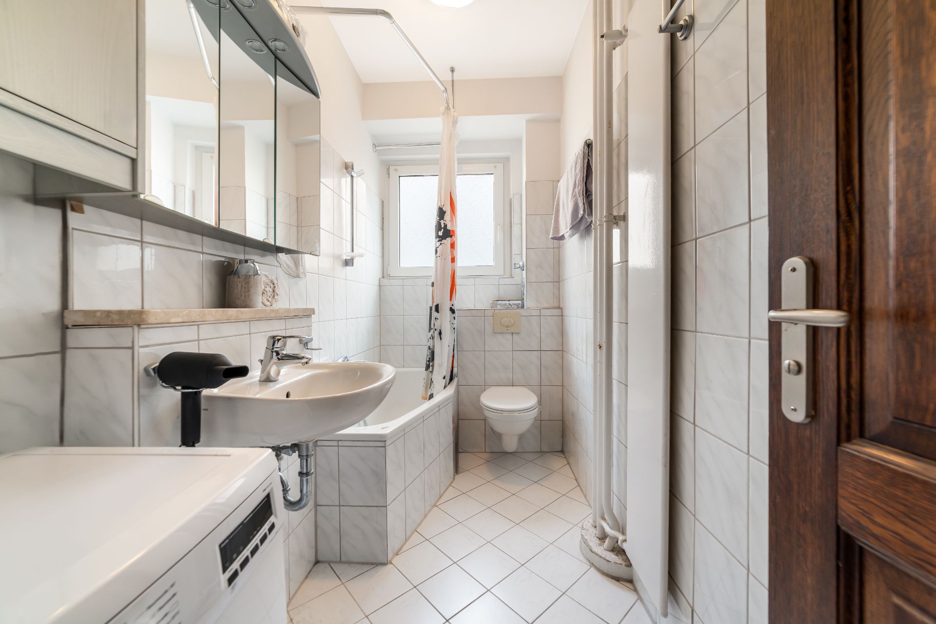 Helles Badezimmer mit Waschbecken, Badewanne, WC, Waschmaschine und Spiegeln.