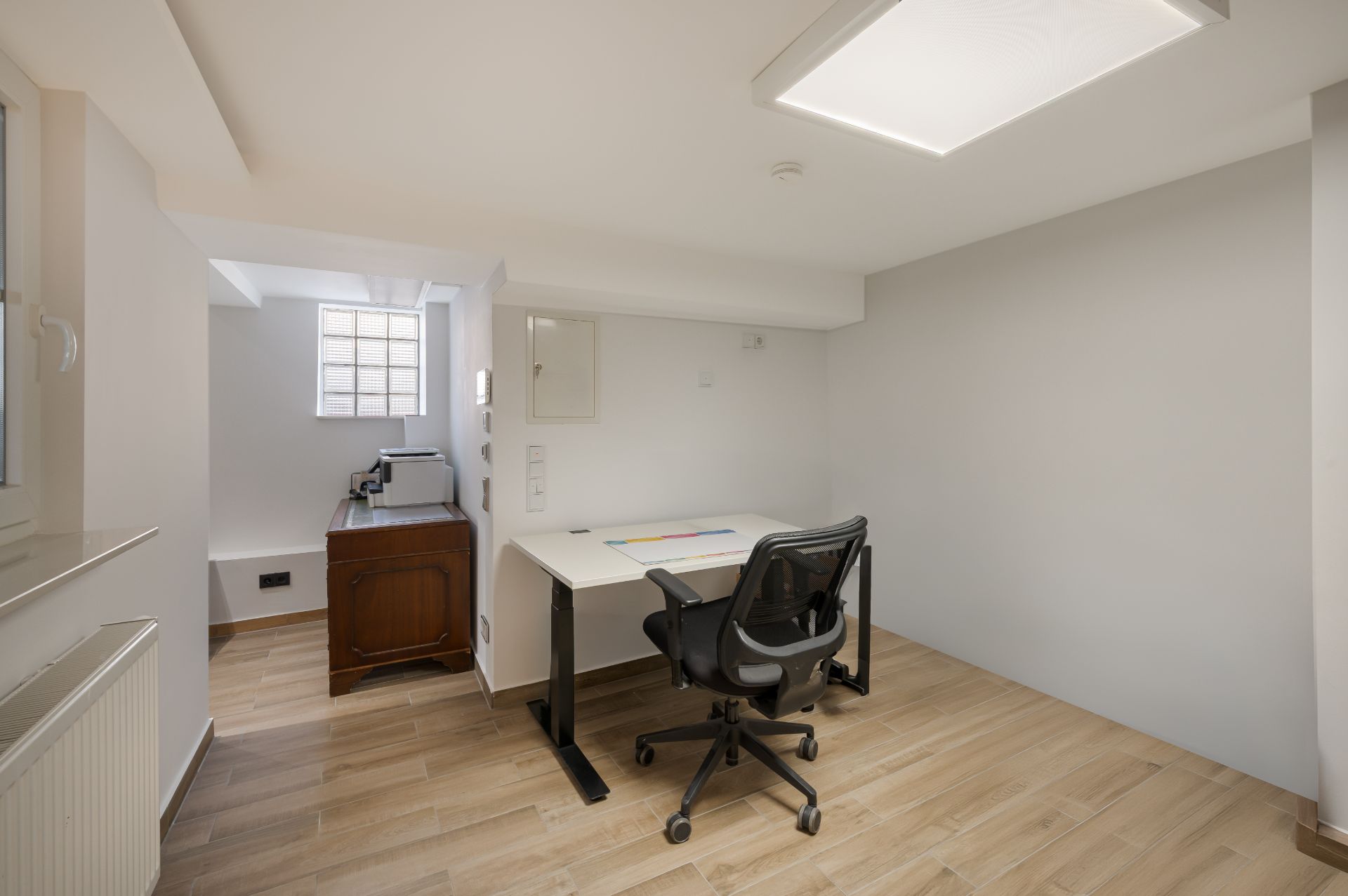Helles Arbeitszimmer mit Schreibtisch, Bürostuhl und Holzboden, Fenster im Hintergrund.