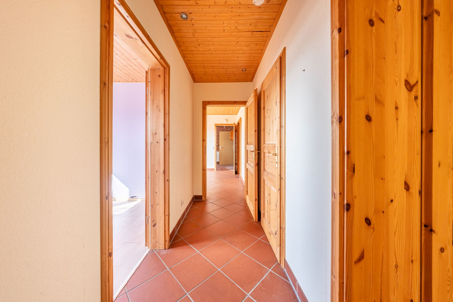 Heller Flur mit Holztüren, Holzdecke und roten Fliesenboden in einem Wohnhaus.