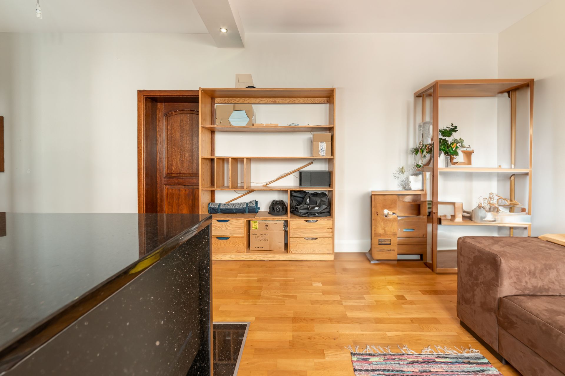 Wohnzimmer mit Holzregalen, braunem Sofa und Pflanzen auf Holzfußboden.