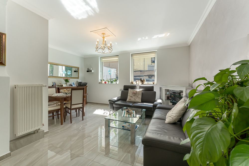 Helles Wohnzimmer mit dunklem Sofa, Glastisch, Esstisch und großen Fenstern.