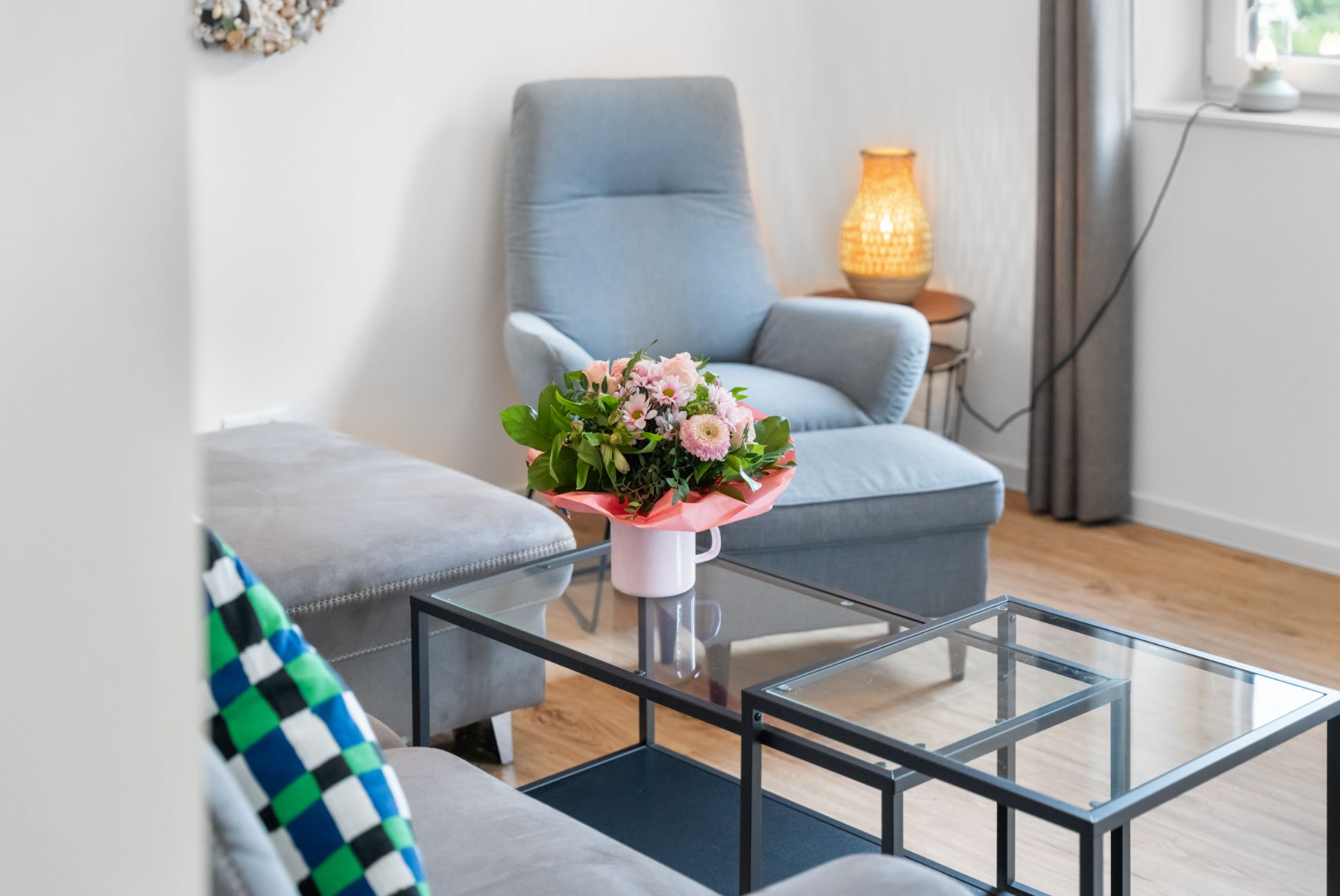 Helles Wohnzimmer mit blauem Sessel, Glastisch und Blumenstrauß auf dem Tisch.
