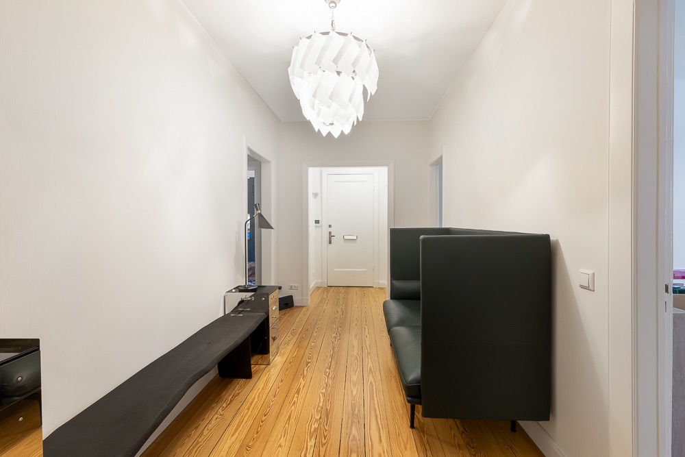 Heller Flur mit Holzboden, Bank, Sofa und modernem Deckenlicht.