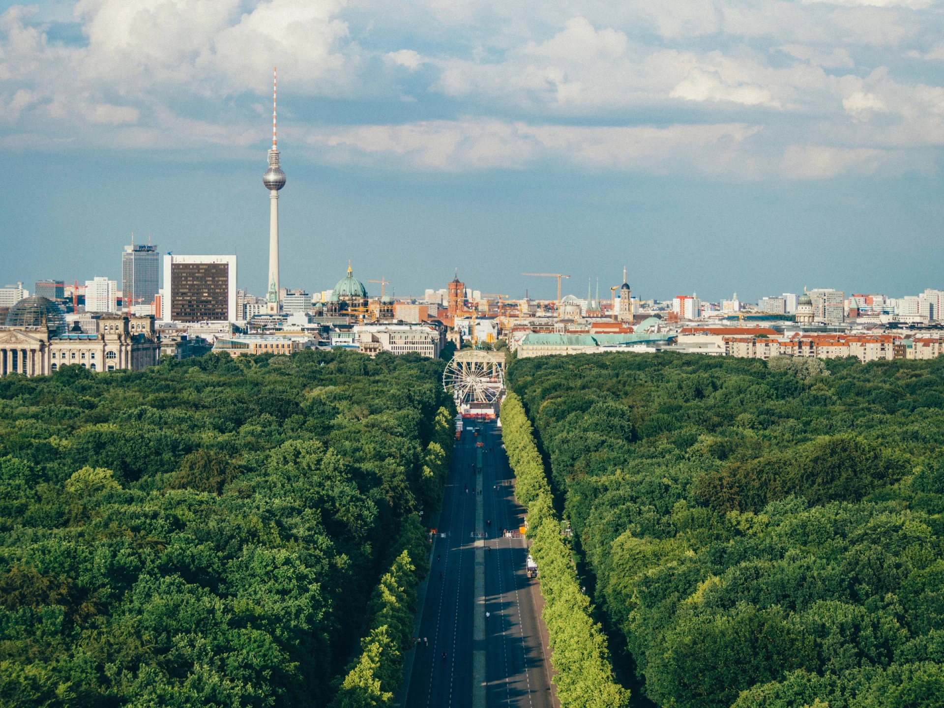 Weitläufiger Stadtpark mit vielen Bäumen, im Hintergrund eine Großstadt mit Fernsehturm.