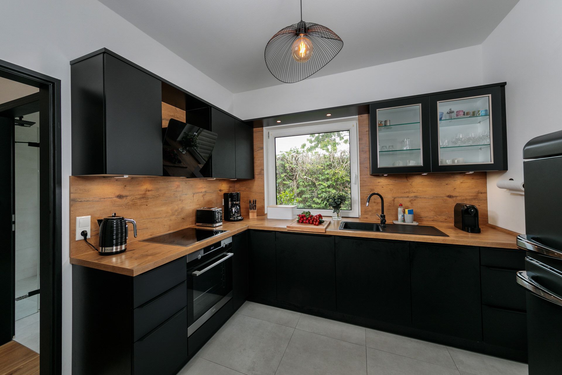 Moderne schwarze Einbauküche mit Holzelementen, großem Fenster und Küchengeräten.