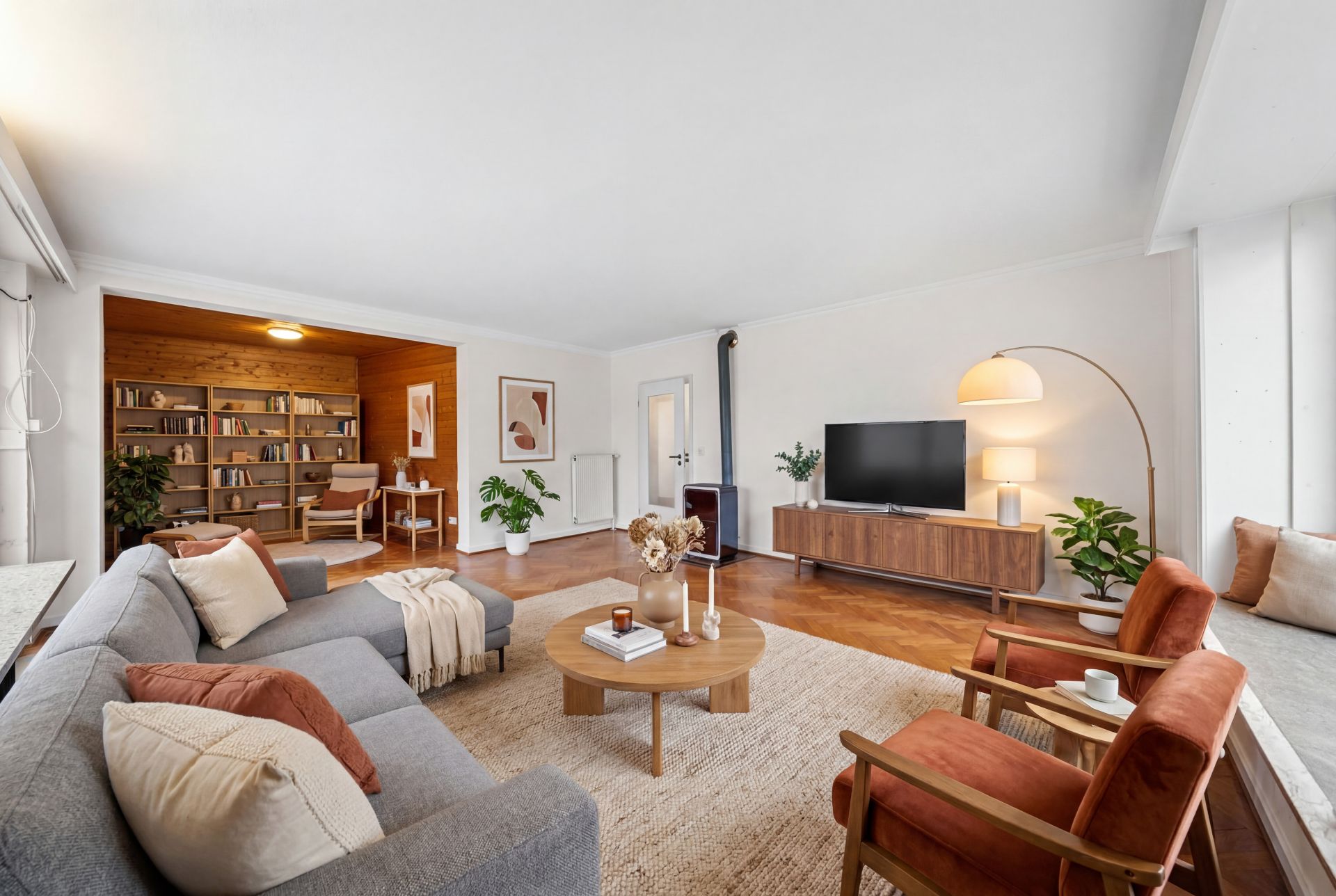 Modernes Wohnzimmer mit Sofa, Sesseln, Couchtisch, Fernseher und großer Bücherwand.