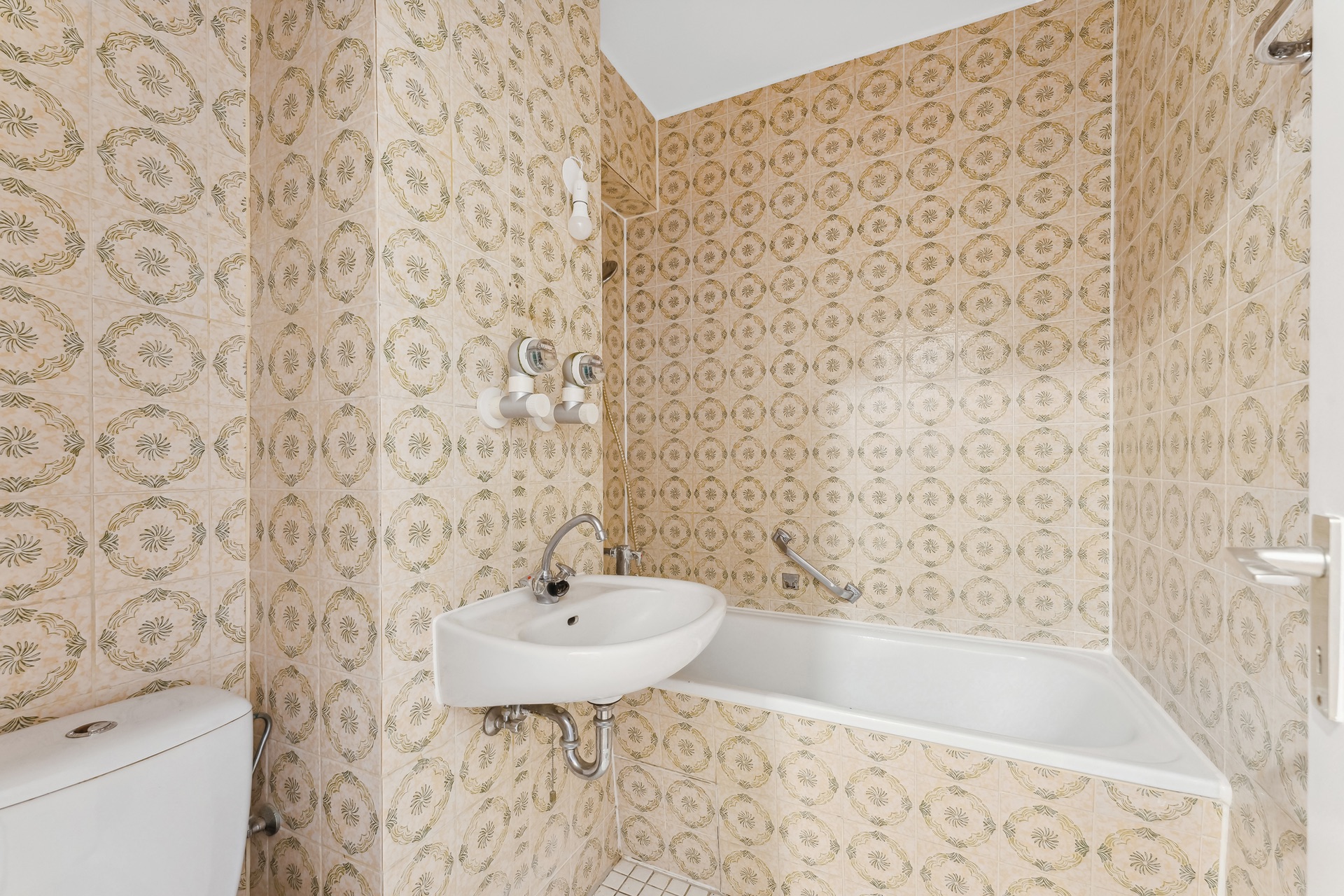 Kleines Badezimmer mit gemusterter Fliesenwand, Badewanne, Waschbecken und Toilette.