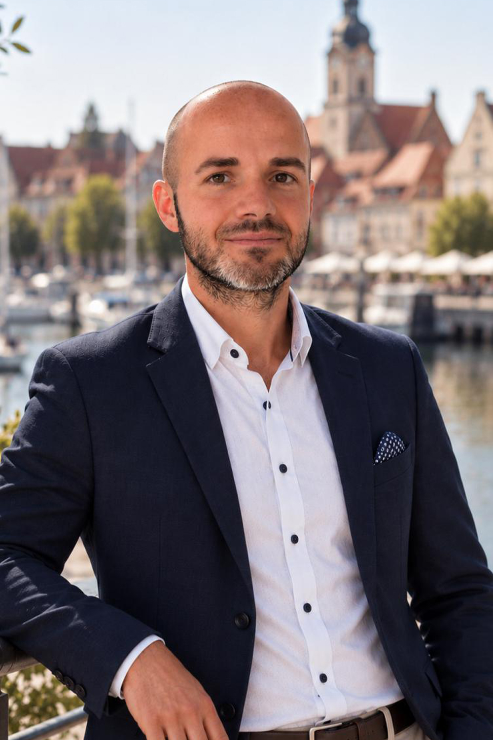 Ein Mann im Anzug steht draußen vor Wasser und historischen Gebäuden.