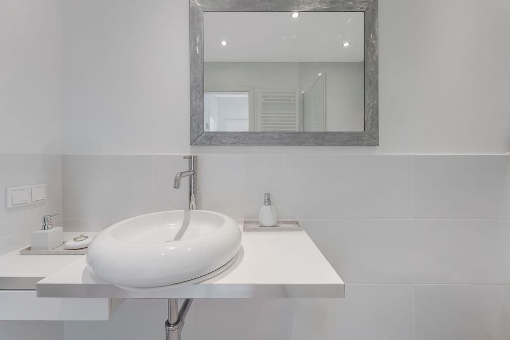 Modernes Badezimmer mit rundem Waschbecken, Spiegel und Seifenspender auf weißem Waschtisch.