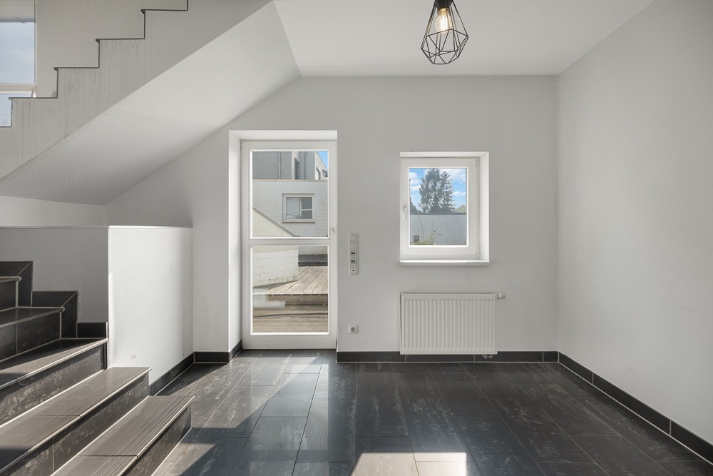 Heller Flur mit schwarzen Fliesen, Treppe, Tür und Fenster in modernem Wohnhaus.