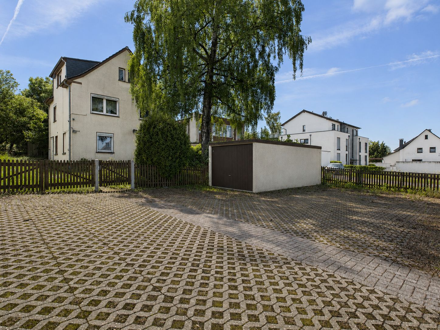 Gepflasterter Parkplatz mit Garage und Wohnhäusern im Hintergrund.