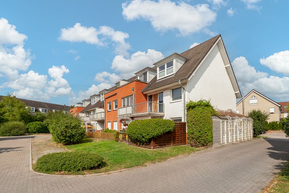 Zweistöckiges Wohnhaus mit Balkon, Vorgarten und Fahrradunterstand an einer ruhigen Straße.