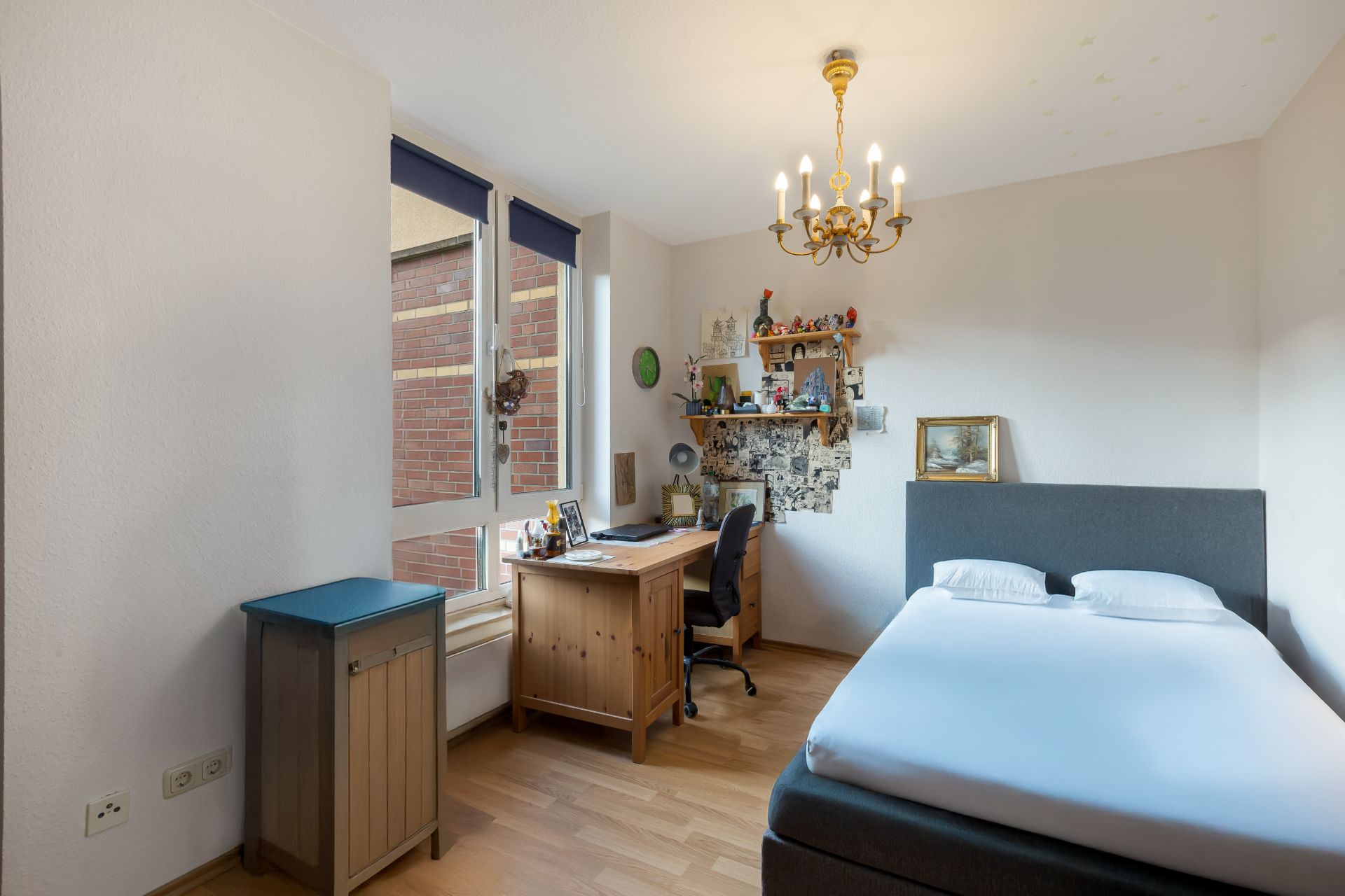 Helles Schlafzimmer mit Bett, Schreibtisch, Regal, Fenster und Holzfußboden.
