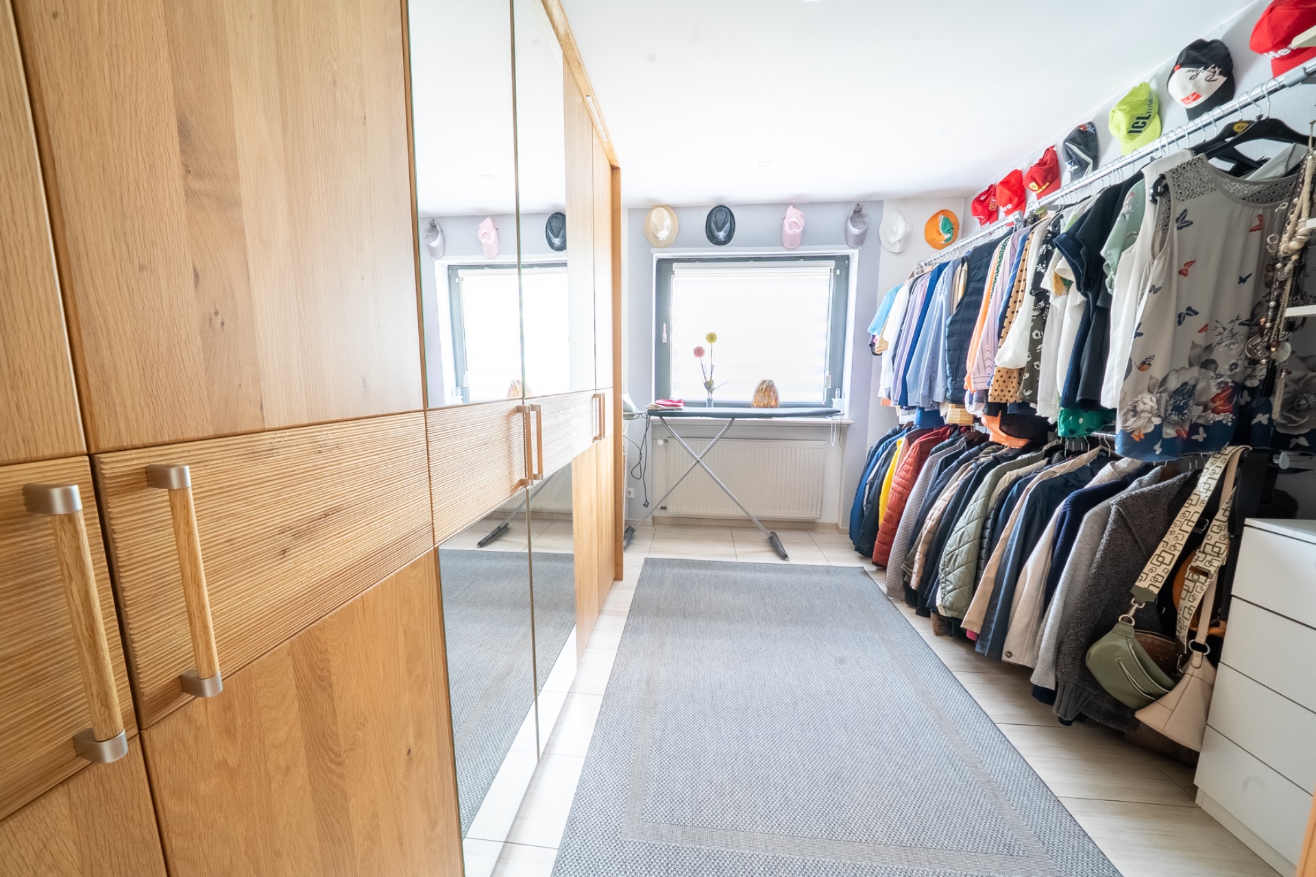 Ankleidezimmer mit Holzschränken, Kleiderstange und Fenster im Hintergrund.