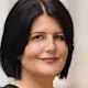 Frau mit dunklen Haaren in schwarzem Kleid steht draußen vor einem Gebäude.