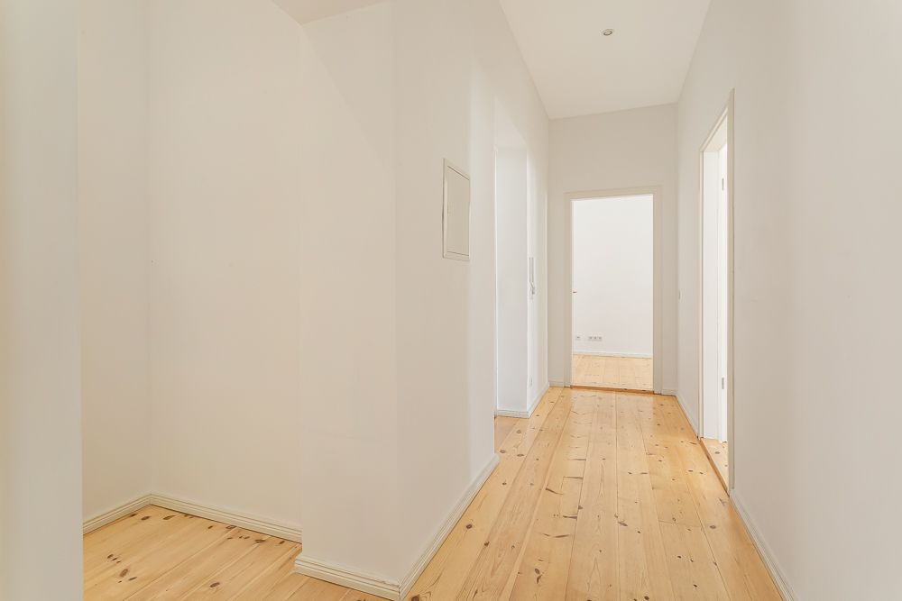 Heller Flur mit Holzboden und weißen Wänden, mehrere Türen führen in andere Räume.