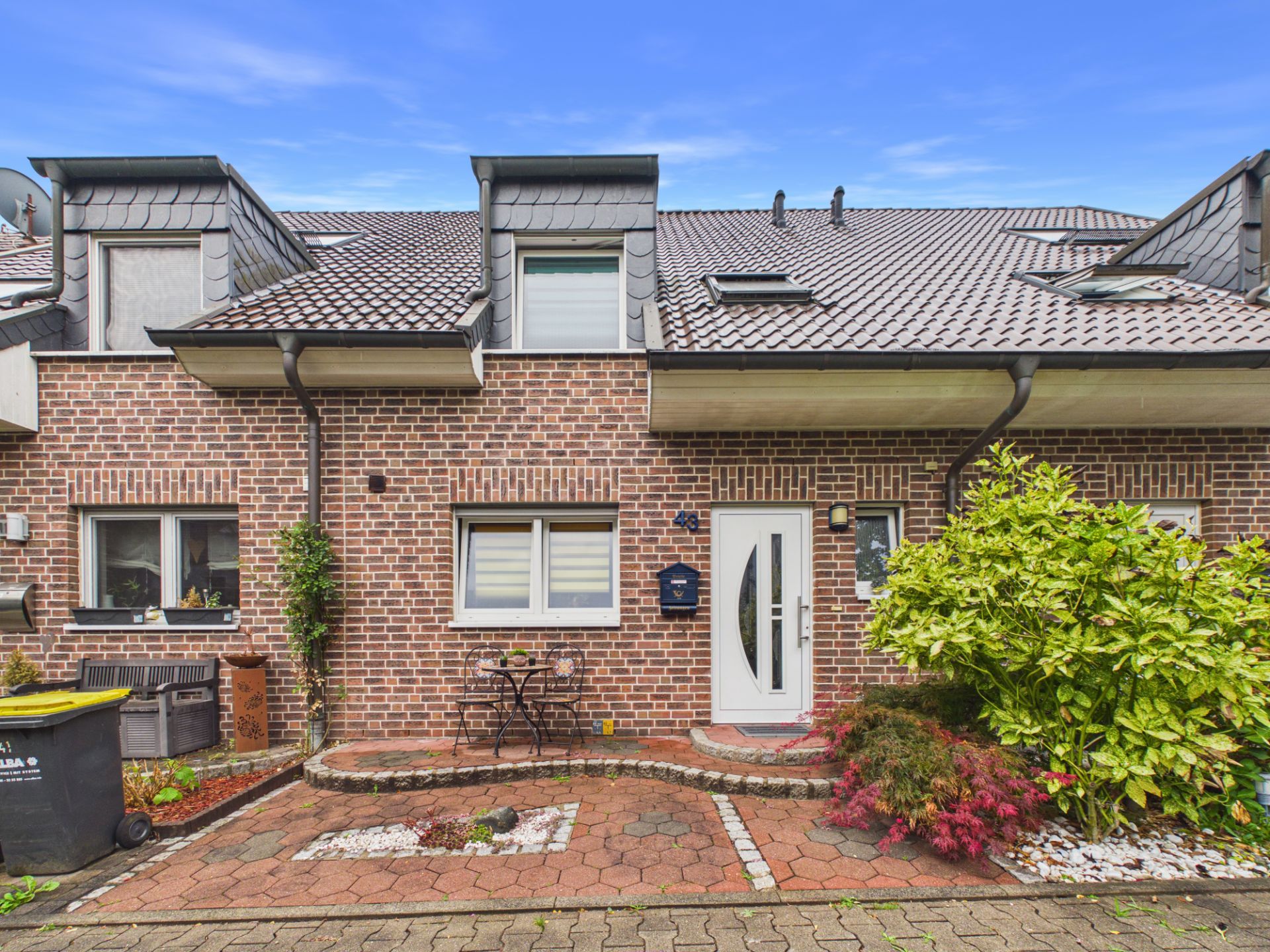Vorderansicht eines Reihenhauses mit Klinkerfassade, kleinem Vorgarten und Sitzgelegenheit.