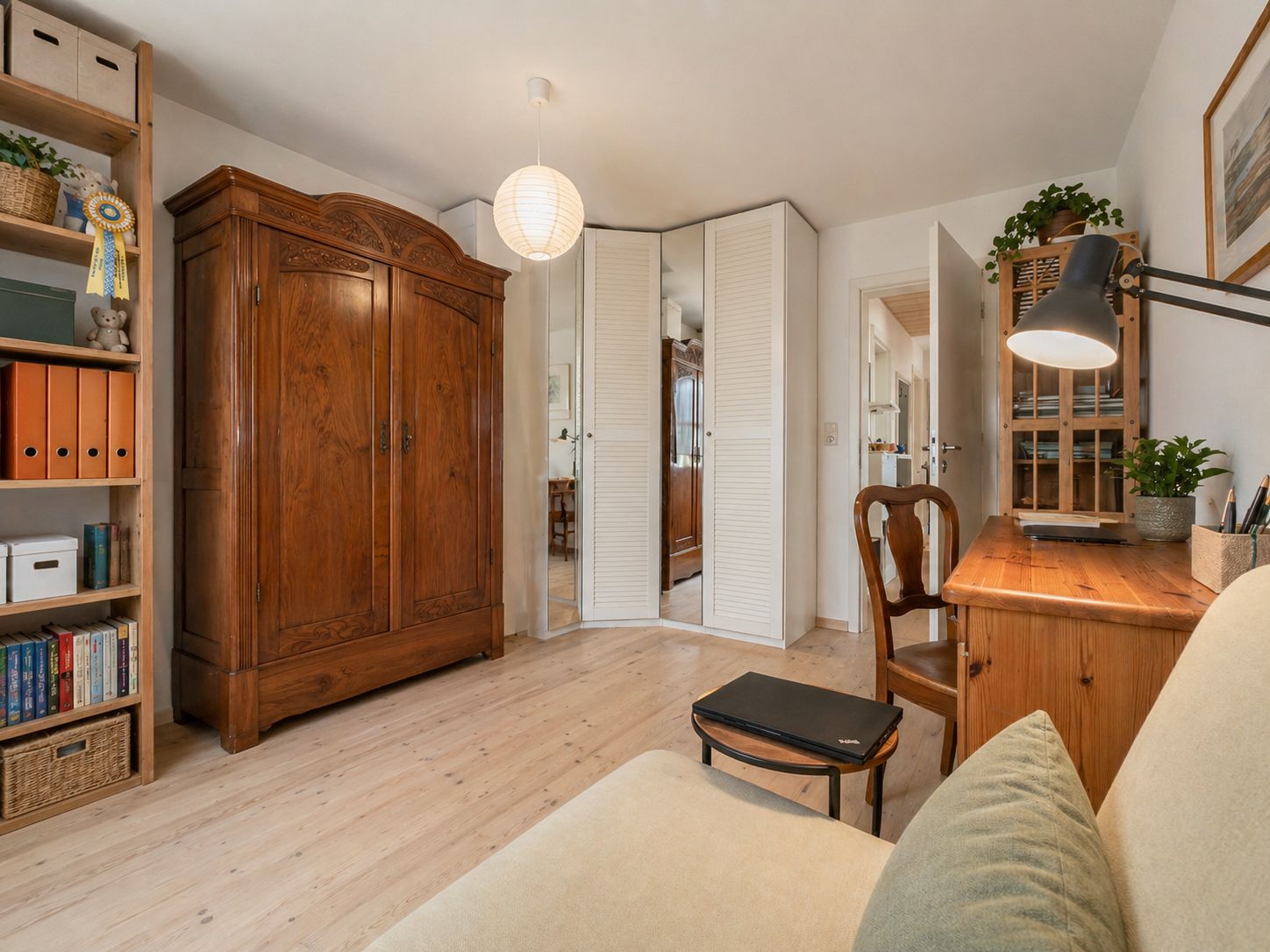 Helles Arbeitszimmer mit Holzschreibtisch, Regal, Sofa und großem Kleiderschrank.